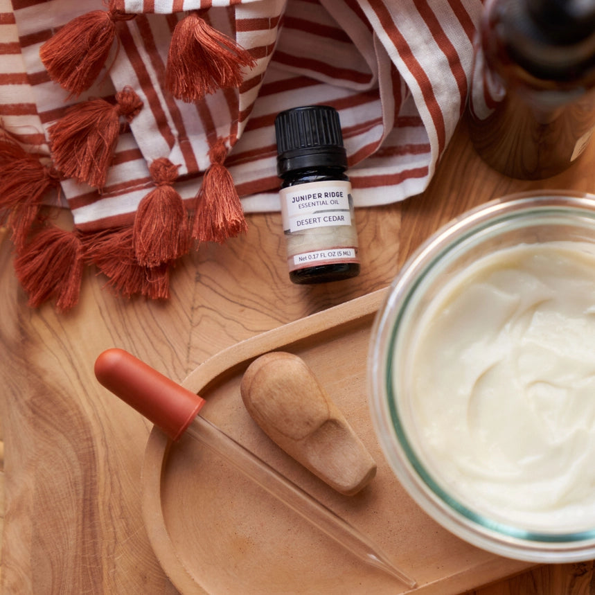 Desert Cedar æterisk olie på bord med tekstil og stearinlys, afslappende hjemmeduft