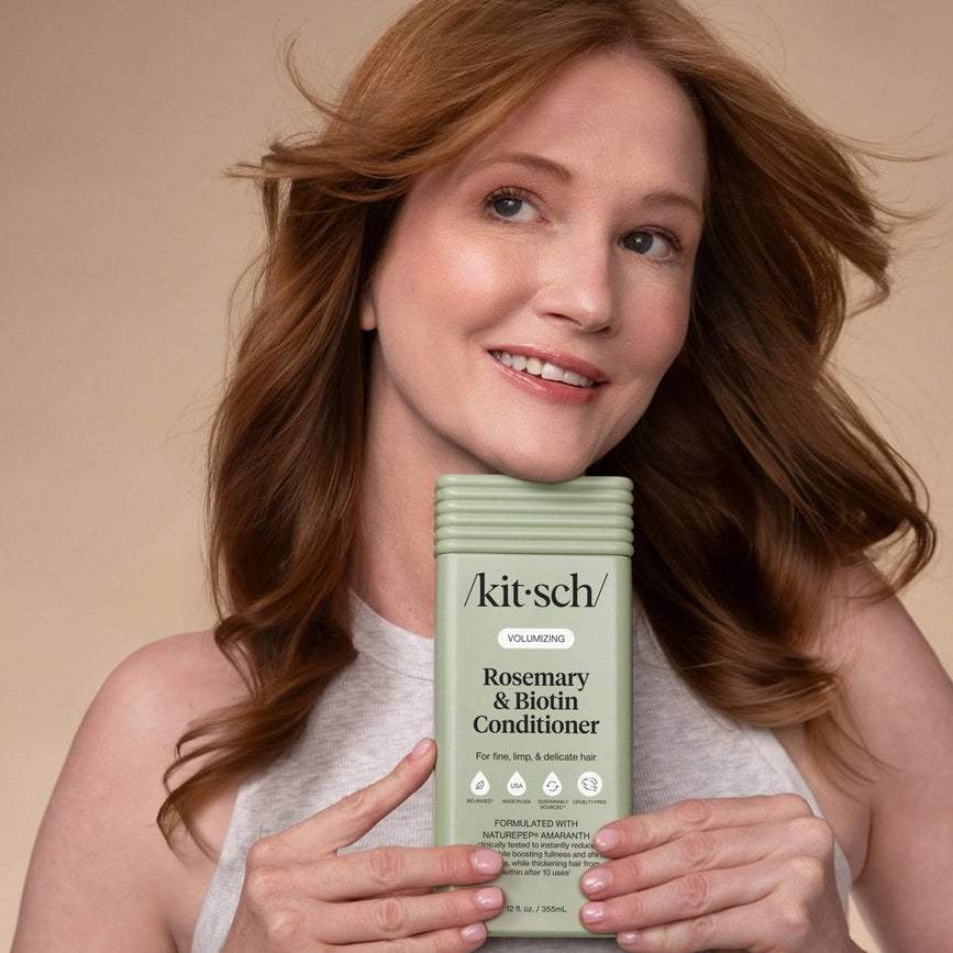 Redhead kvinde med voluminøst, glansfuldt hår, holder KITSCH balsam med rosmarin og biotin, beige baggrund