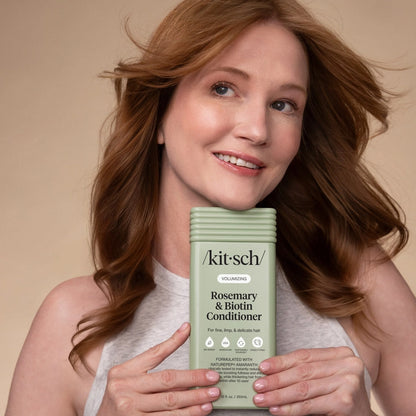 Redhead kvinde med voluminøst, glansfuldt hår, holder KITSCH balsam med rosmarin og biotin, beige baggrund