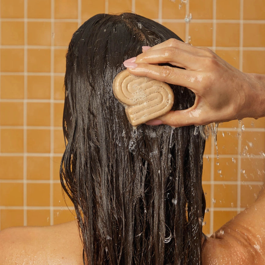 Person bruger shampoo bar i brusebad, blødgør og renser hår, miljøvenlig