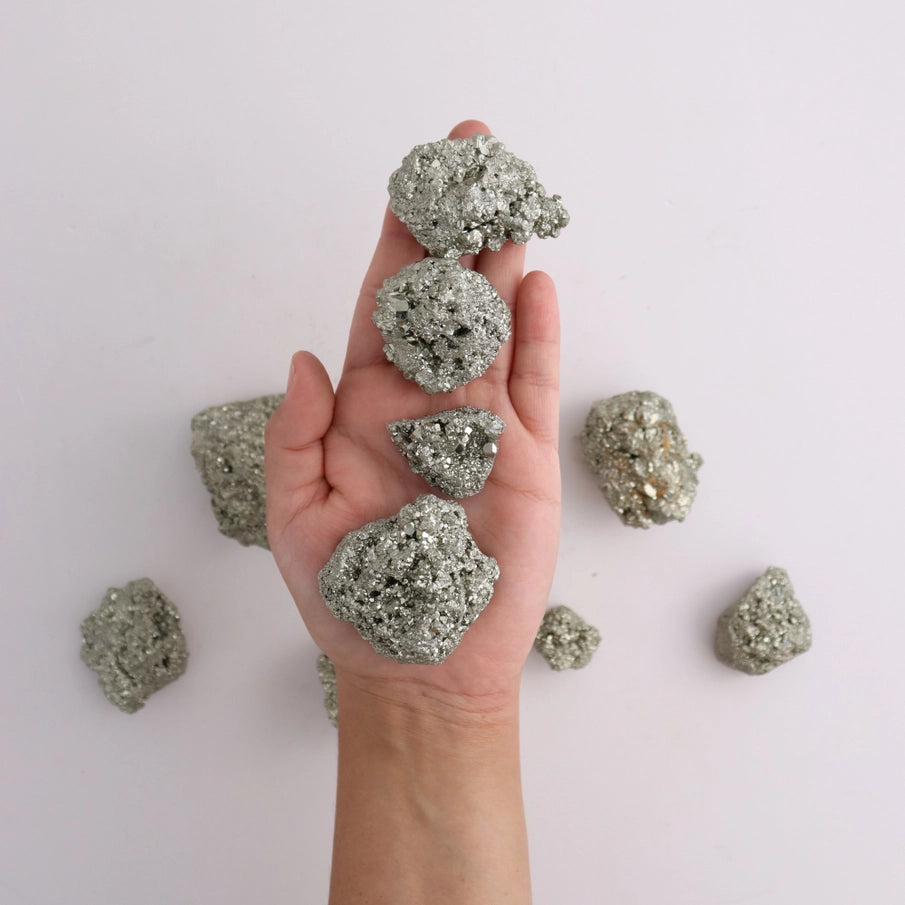 Hånd holder pyrit krystaller med gyldent metallisk skær, spirituel dekoration og overflod